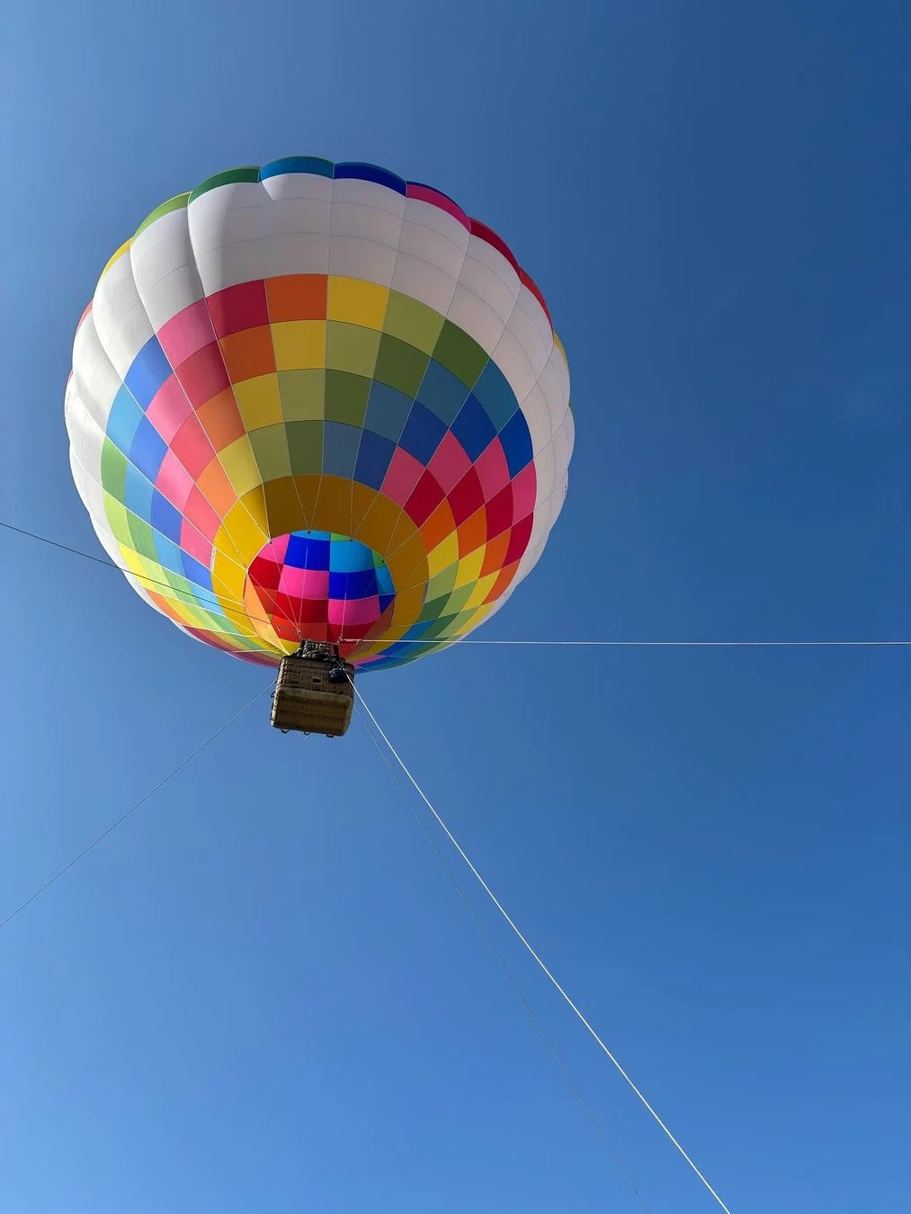 青い空を背景に、色とりどりの四角いパッチワーク模様が特徴的な熱気球が浮かんでいる様子